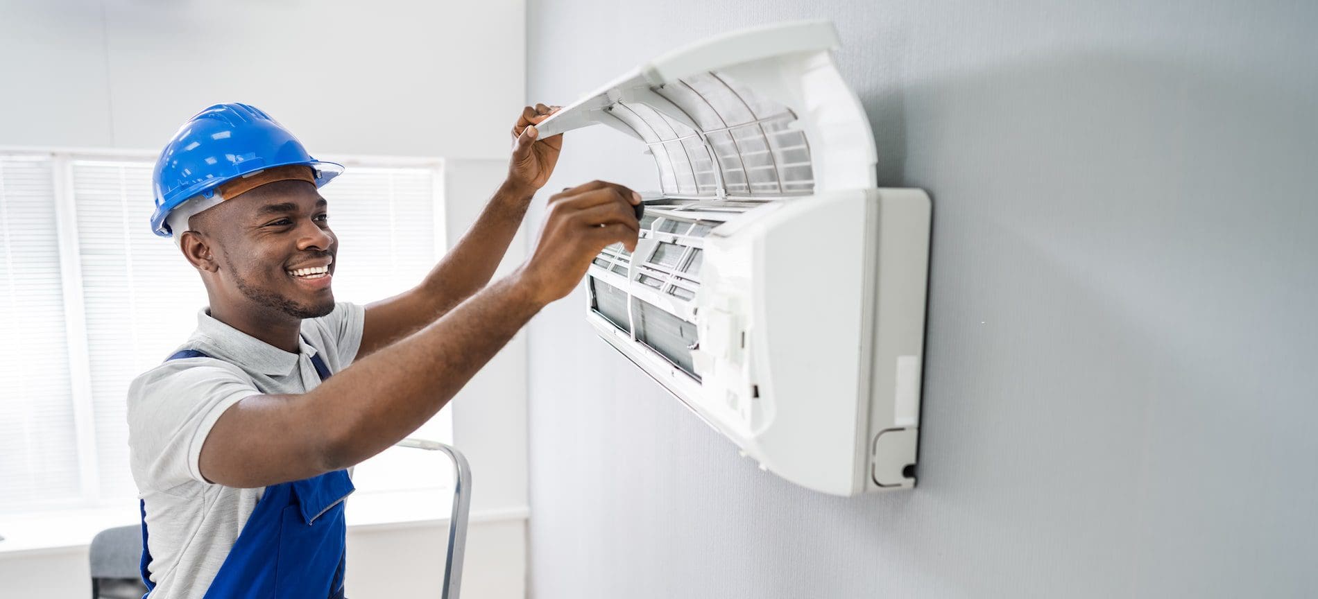 An expert in a hard hat and blue shirt diligently fixes an air conditioner. Our AC Repair in Lafayette ensures swift and effective cooling system fixes.